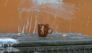 Fotografi af et skåret kaffekrus på et telefonskab med ølkapsler.