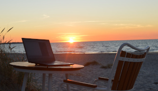Fotografi af en strand med en laptop på et bord i solnedgangen.